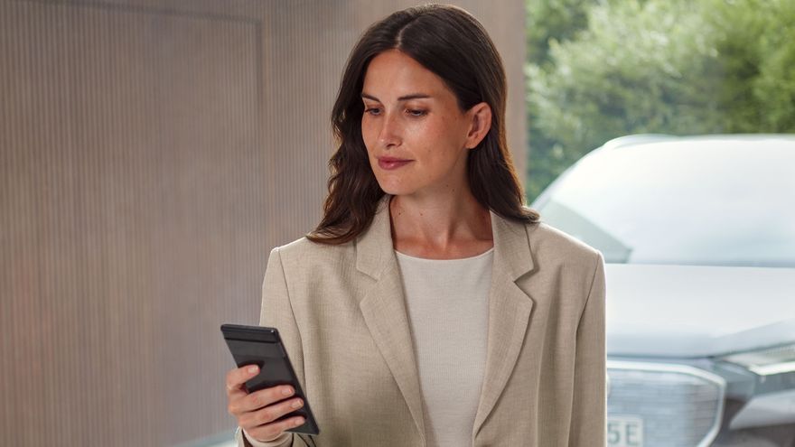 Eine Frau blickt auf ihr Smartphone. Durch die Scheibe im Hintergrund ist ein Audi zu sehen.