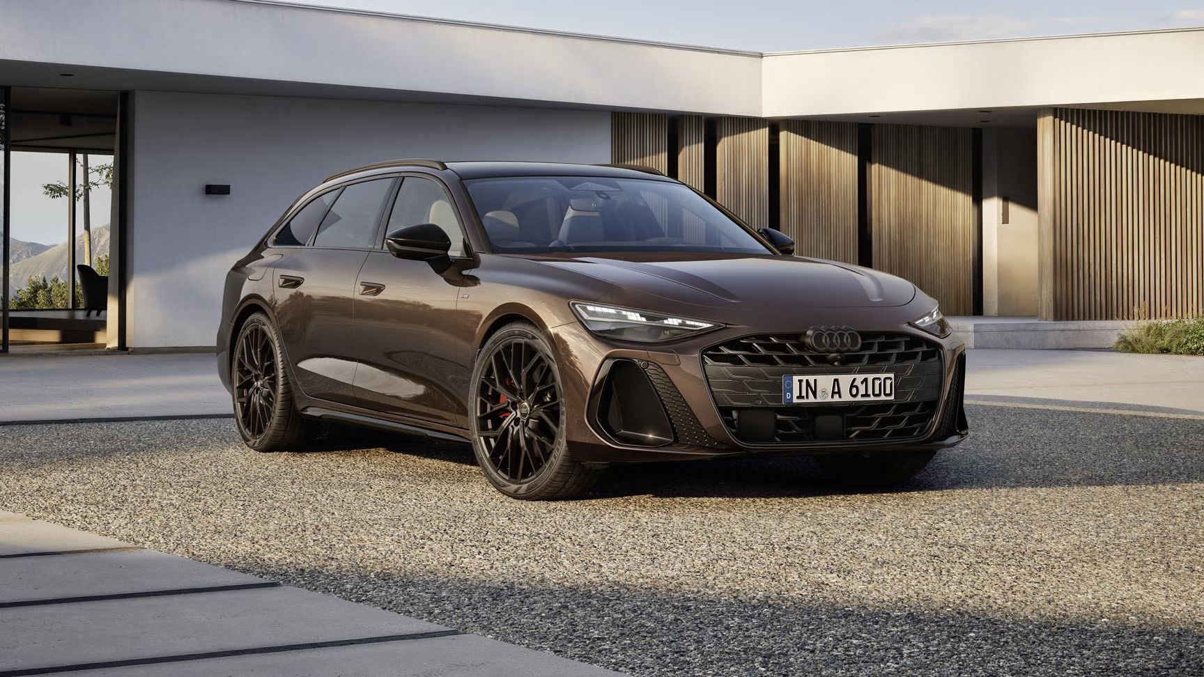 Der A6 Avant steht im schrägen Frontprofil auf einer Kiesfläche vor einem modernen Haus. Die Frontscheinwerfer des Fahrzeugs zeigen eine Lichtsignatur.