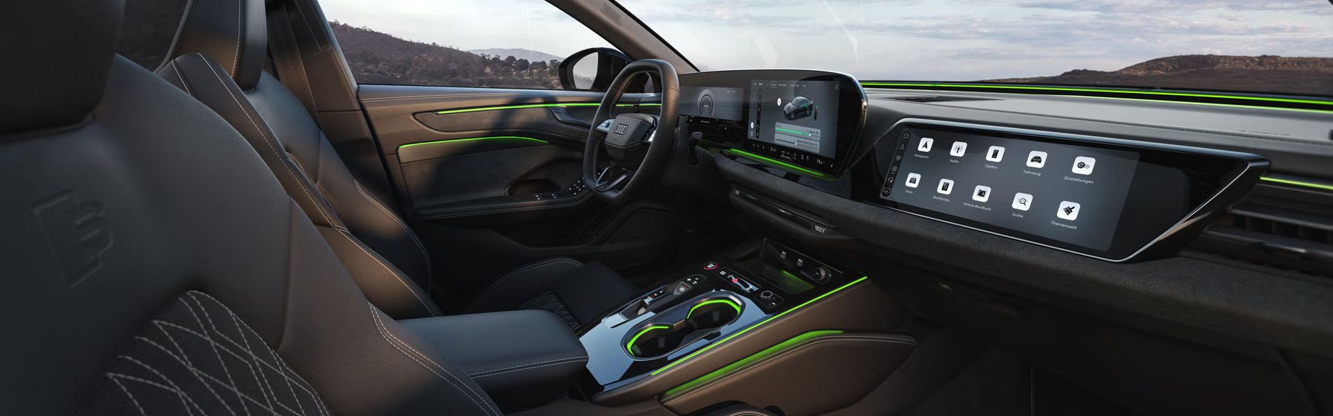 Das Cockpit der A6 Limousine e-hybrid aus Beifahrerperspektive. Der Fokus liegt dabei auf dem Lenkrad sowie den Panorama-Displays und dem grünen Ambiente-Licht.