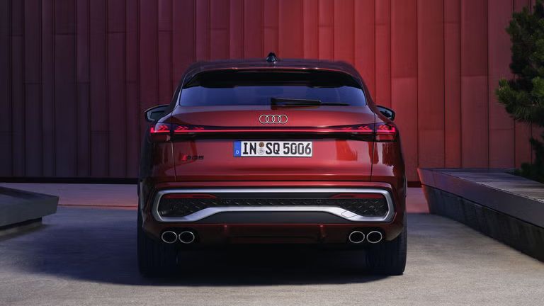 Heckprofil des roten SQ5 Sportback vor einer Gebäudefassade, die vom Fahrzeug rot angeleuchtet wird.