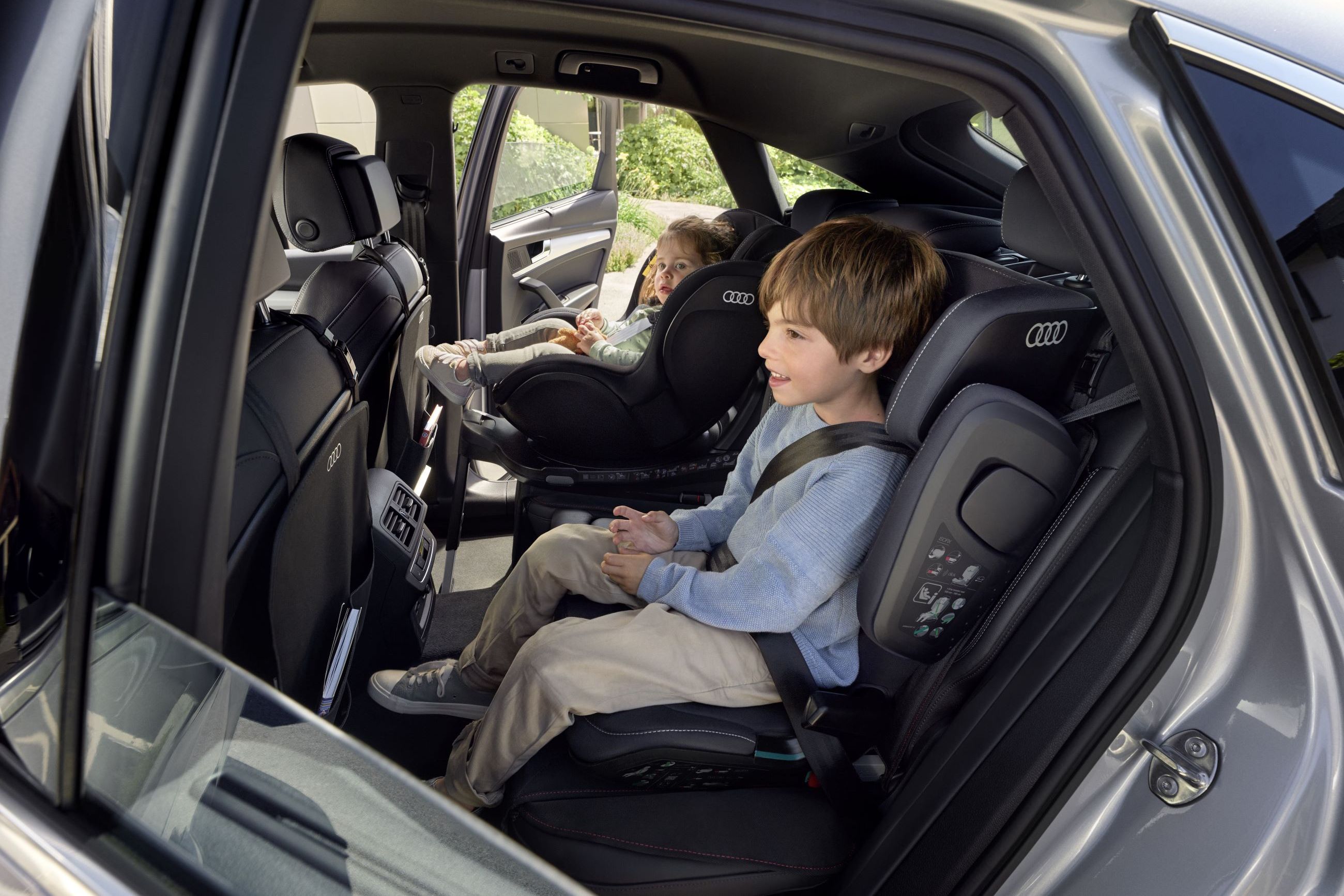 Zwei kleine Kinder in Kindersitzen auf dem Rücksitz von einem Audi.
