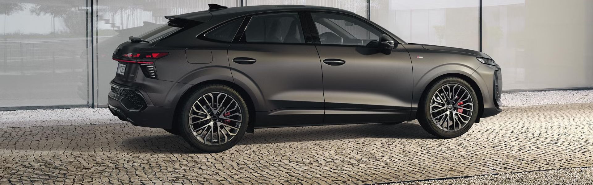 Der Q3 Sportback parkt vor dem Treppengeländer eines Gebäudes auf einem gepflasterten Weg.