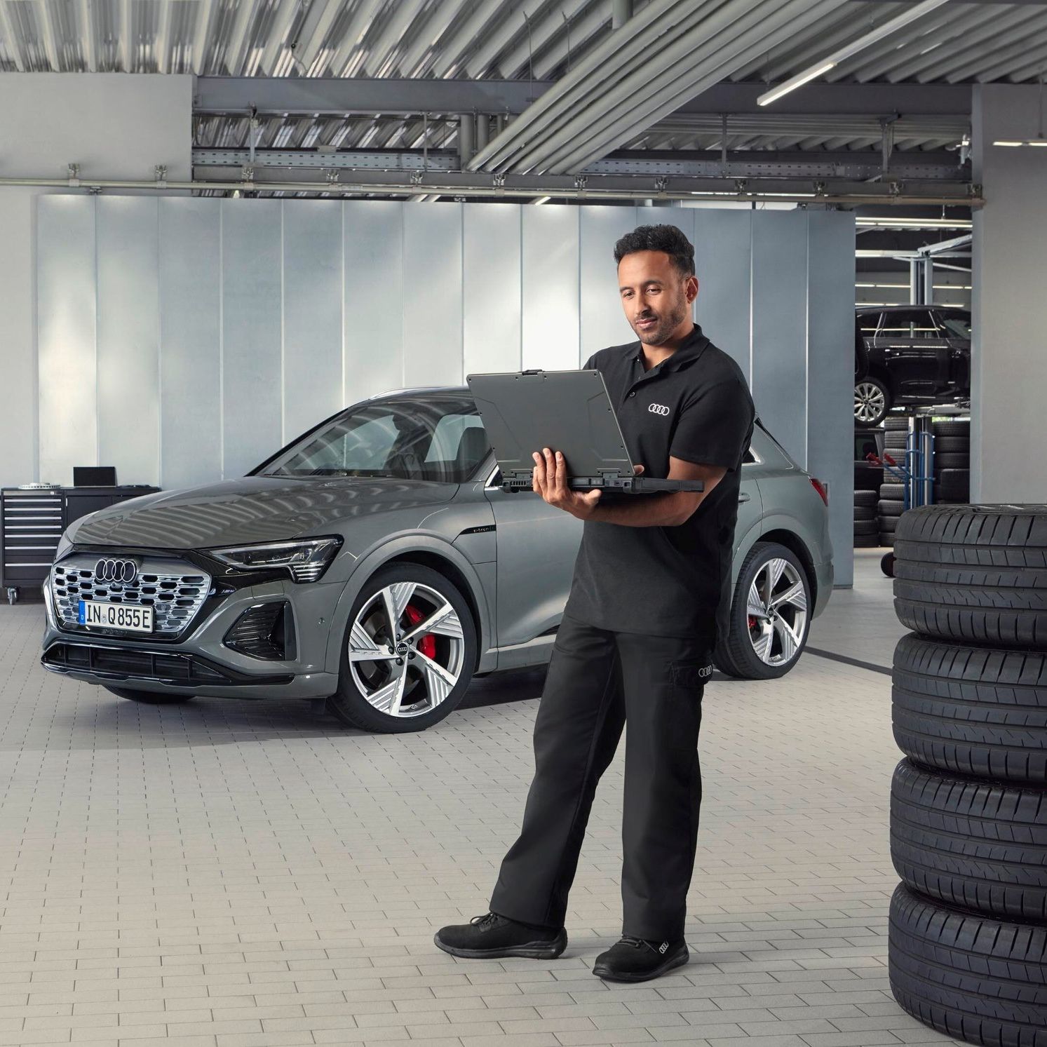 Ein Audi Service Mitarbeiter steht neben gestapelten Reifen und blickt auf sein Notebook.