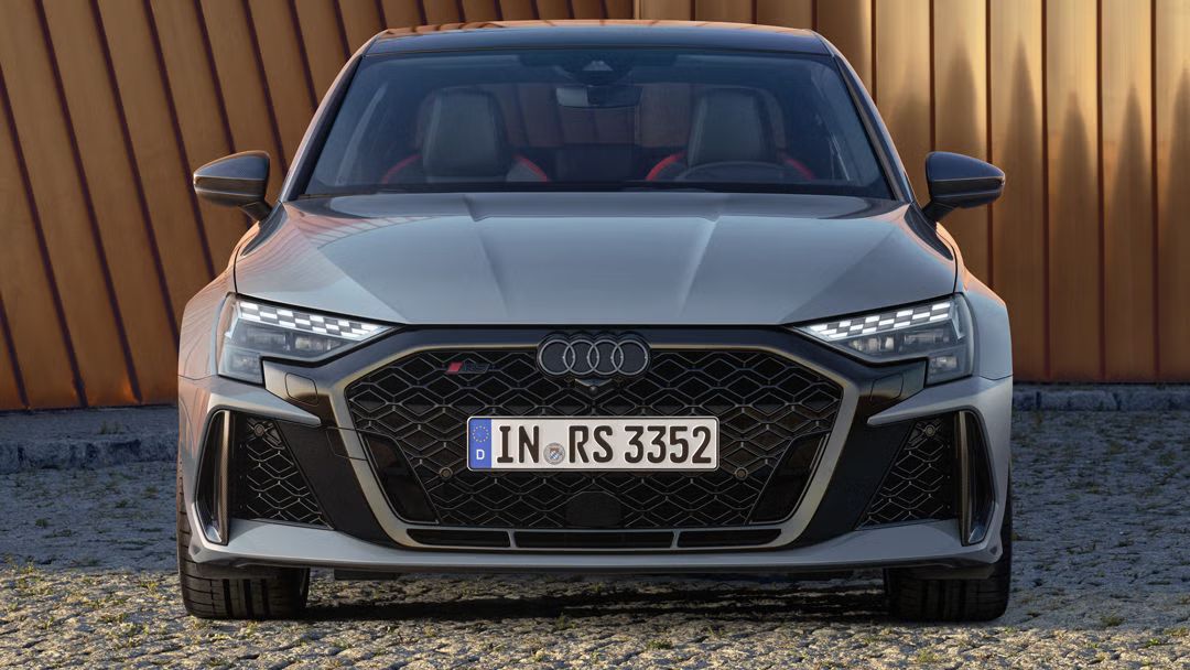 Die RS 3 Limousine parkend auf Kopfsteinpflaster, im Hintergrund Umrisse eines modernen Gebäudes.