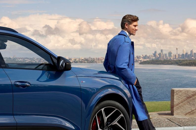 Mann leht an Audi und genießt die Aussicht auf die Stadt