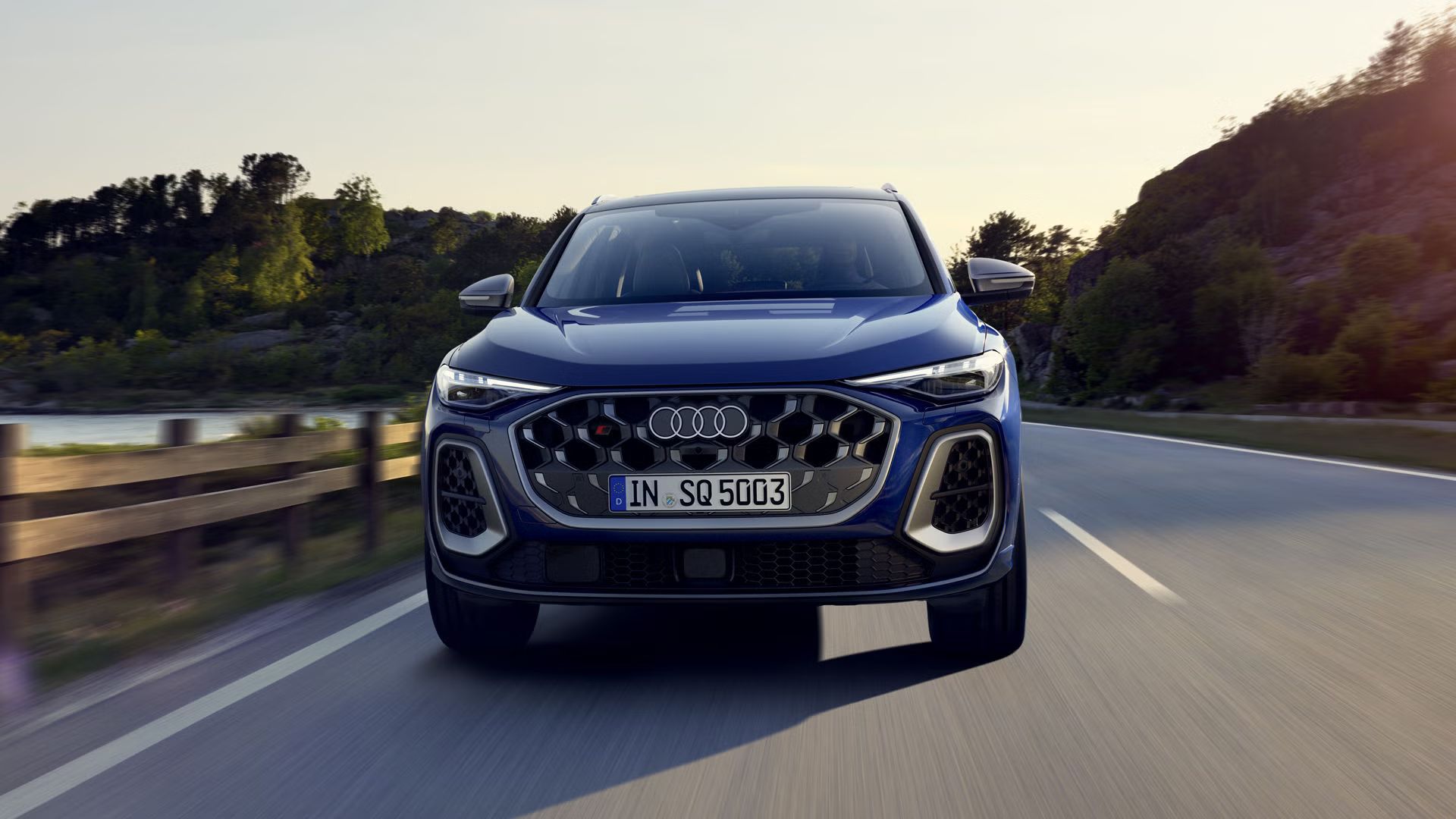 Frontprofil des SQ5 SUV in dunkelblau, welcher auf einer Straße durch die Natur fährt. Am Steuer sitzt eine junge Frau.