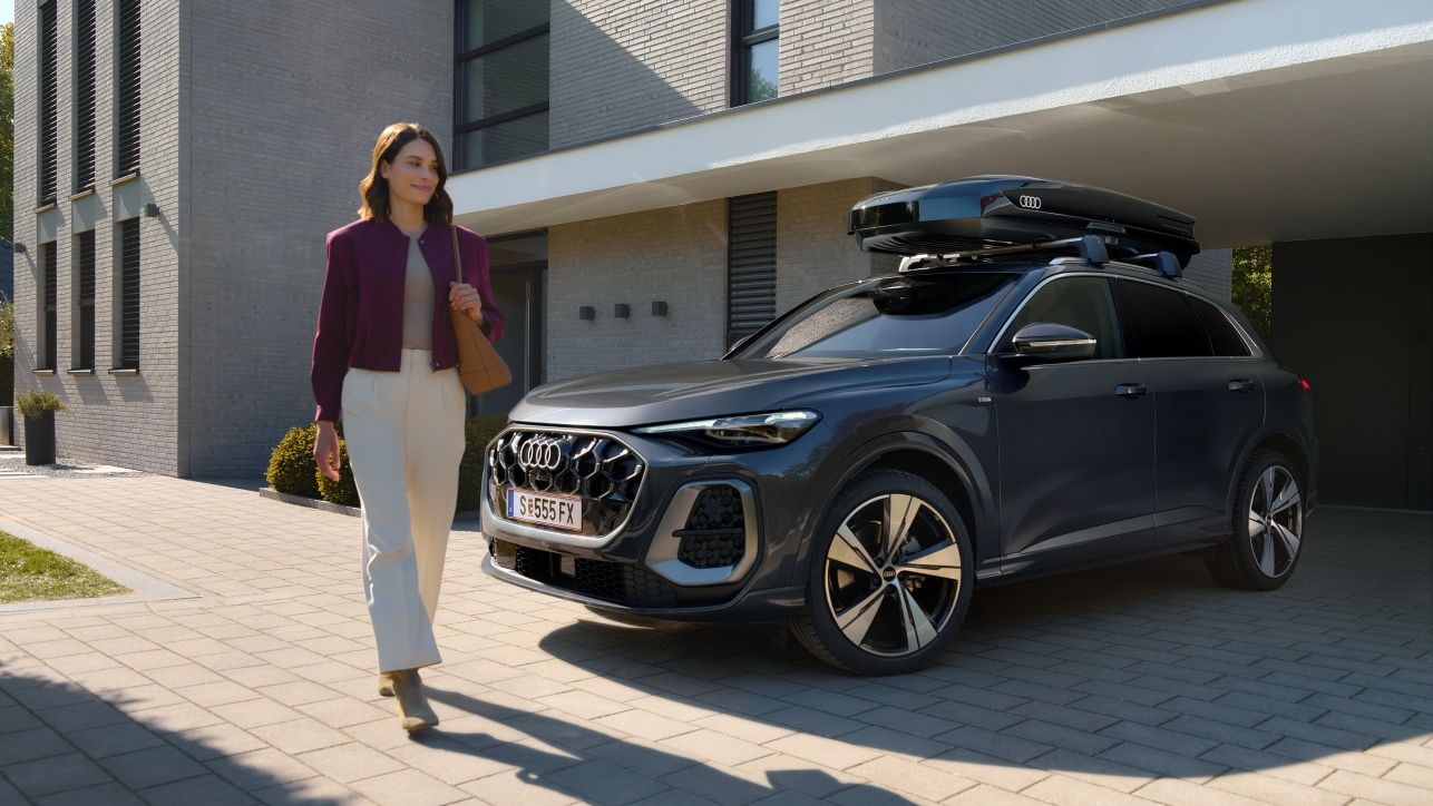 Frau passiert lächelnd einen in der Hauseinfahrt parkenden Audi Q5 mit Dachbox