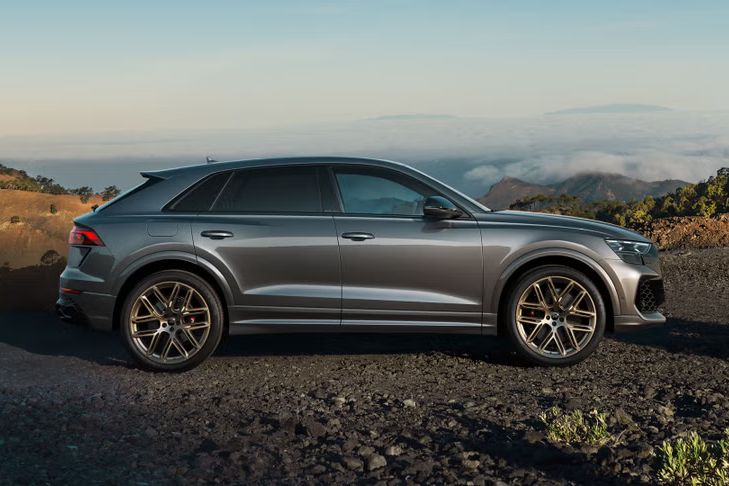 Der RS Q8 SUV in Seitenansicht auf einem Schotterweg, umrahmt von kargen Felsen. Im Hintergrund sind Wolkenbänder zu erkennen.