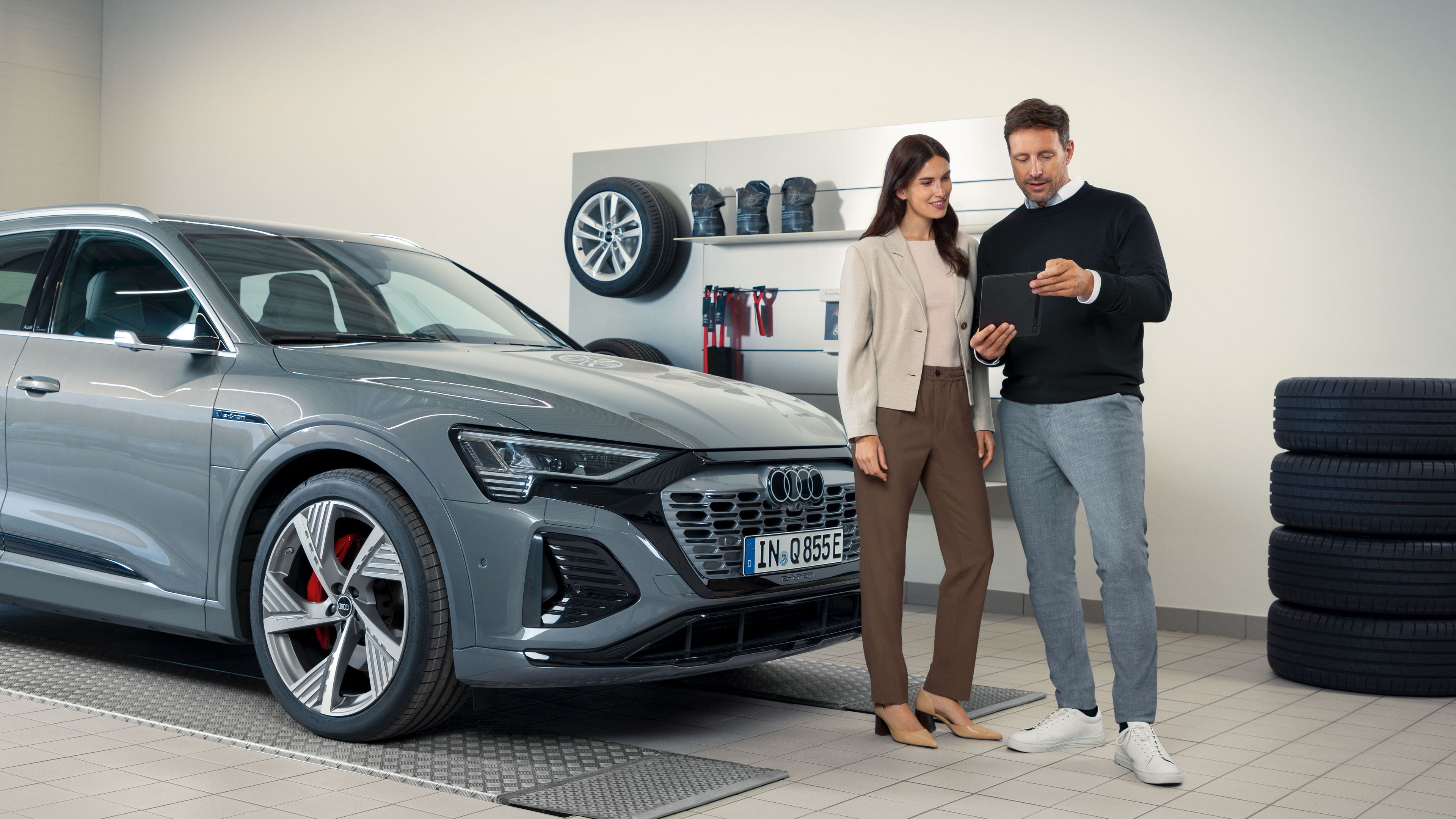 Ein Audi Service Mitarbeiter im Gespräch mit einer Kundin, beide stehen vor einem Audi Elektroauto