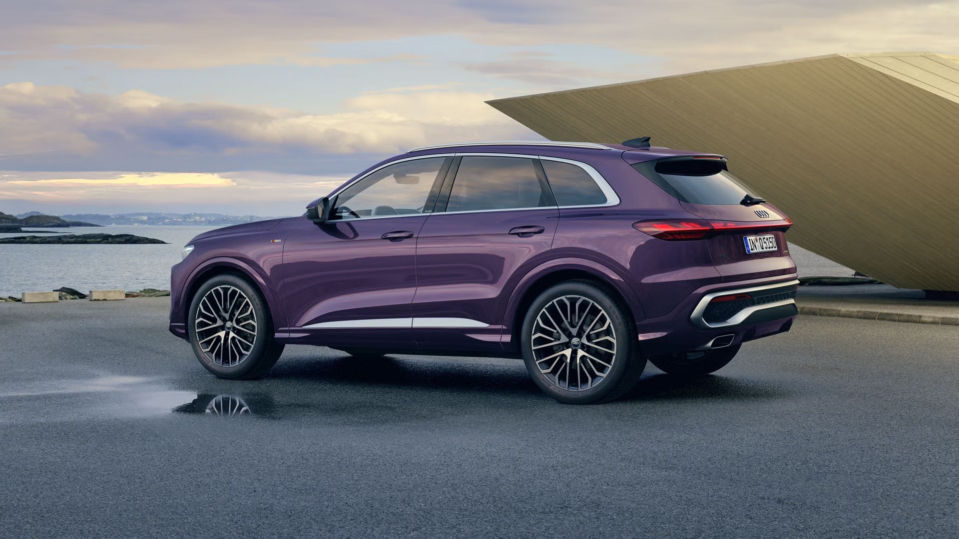 Der Q5 SUV mit der Individuallackierung Merlin Perleffekt steht im schrägen Seitenprofil an der Küste. Rechts von ihm befindet sich ein futuristisches Gebäude.