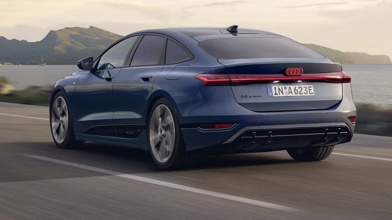 Der A6 Sportback e-tron aus schräger Heckansicht fährt eine Straße parallel zum Ufer entlang. Im Hintergrund sind Berge zu erkennen. 