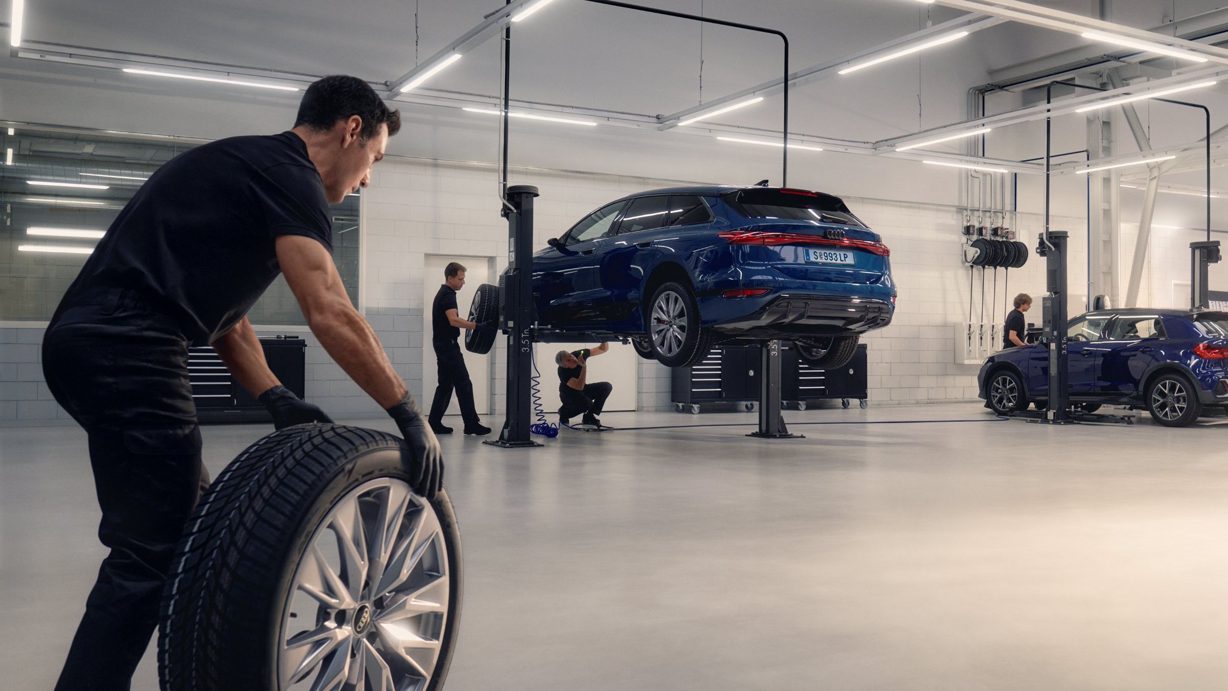 Ein Audi Mechaniker rollt ein Winterkomplettrad in Richtung eines Audi auf einer Hebebühne.