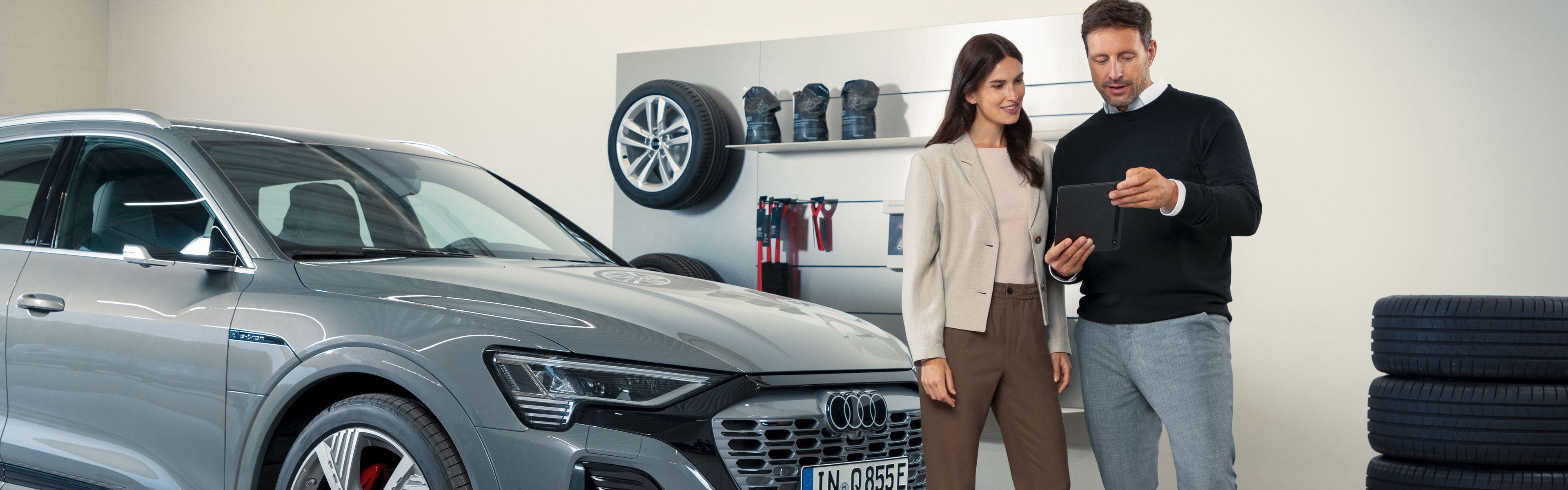 Ein Audi Service Mitarbeiter im Gespräch mit einer Kundin, beide stehen vor einem Audi Elektroauto