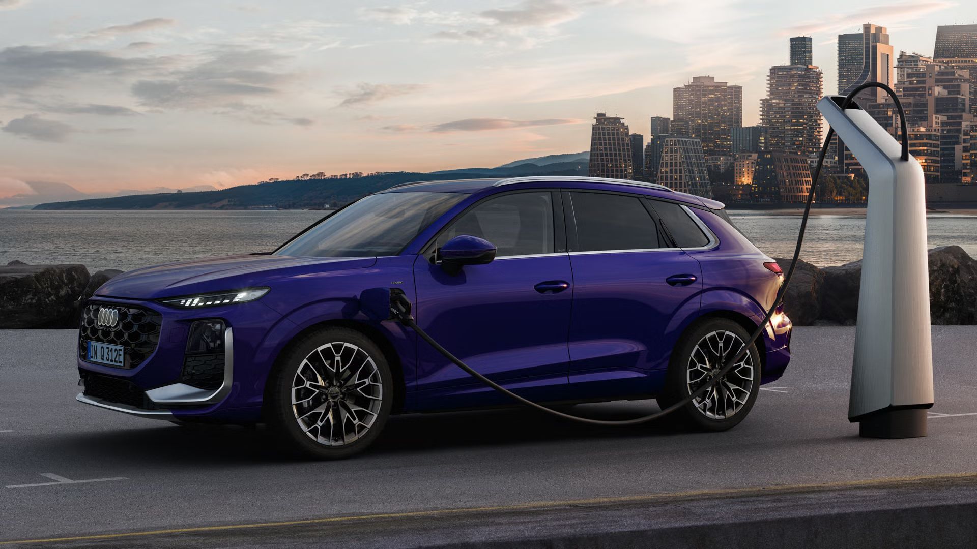 Ein Q3 SUV e-hybrid im Samtviolett Perleffekt an einer Ladestation, im Hintergrund die Skyline einer Küstenstadt.