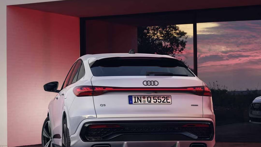 Heckansicht des Q5 Sportback e-hybrid, welcher vor bodentiefen Fenstern eines Hauses steht und diese mit seinen Scheinwerfern anleuchtet.