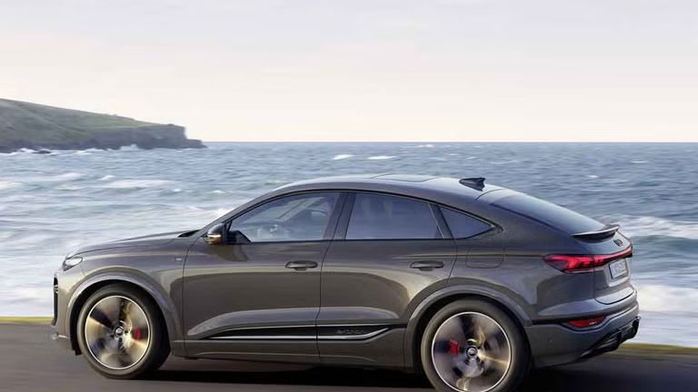 Seitliche Aufnahme des Q6 Sportback e-tron, welcher auf einer Straße entlang des Meeres fährt.