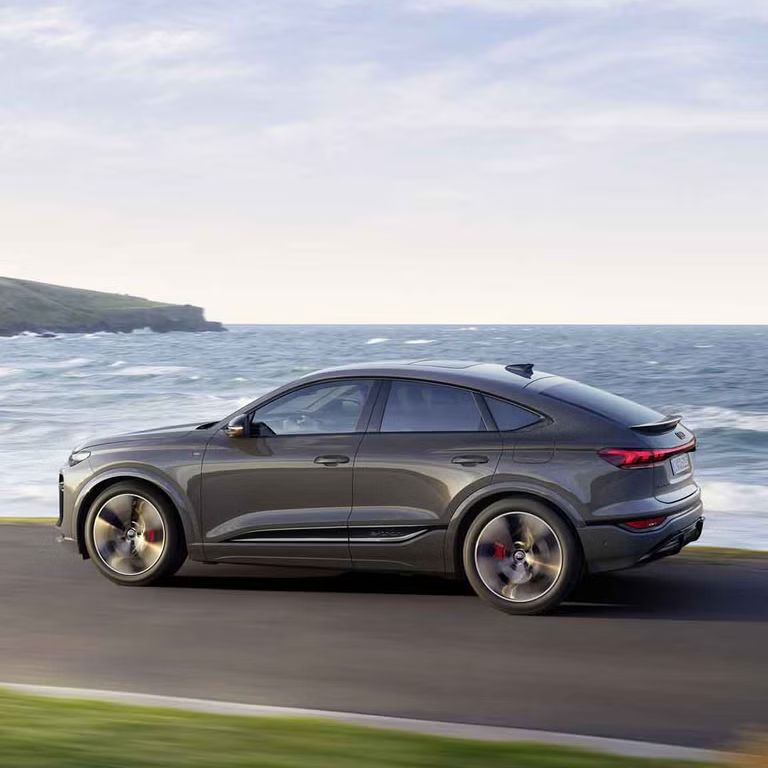 Seitliche Aufnahme des Q6 Sportback e-tron, welcher auf einer Straße entlang des Meeres fährt.