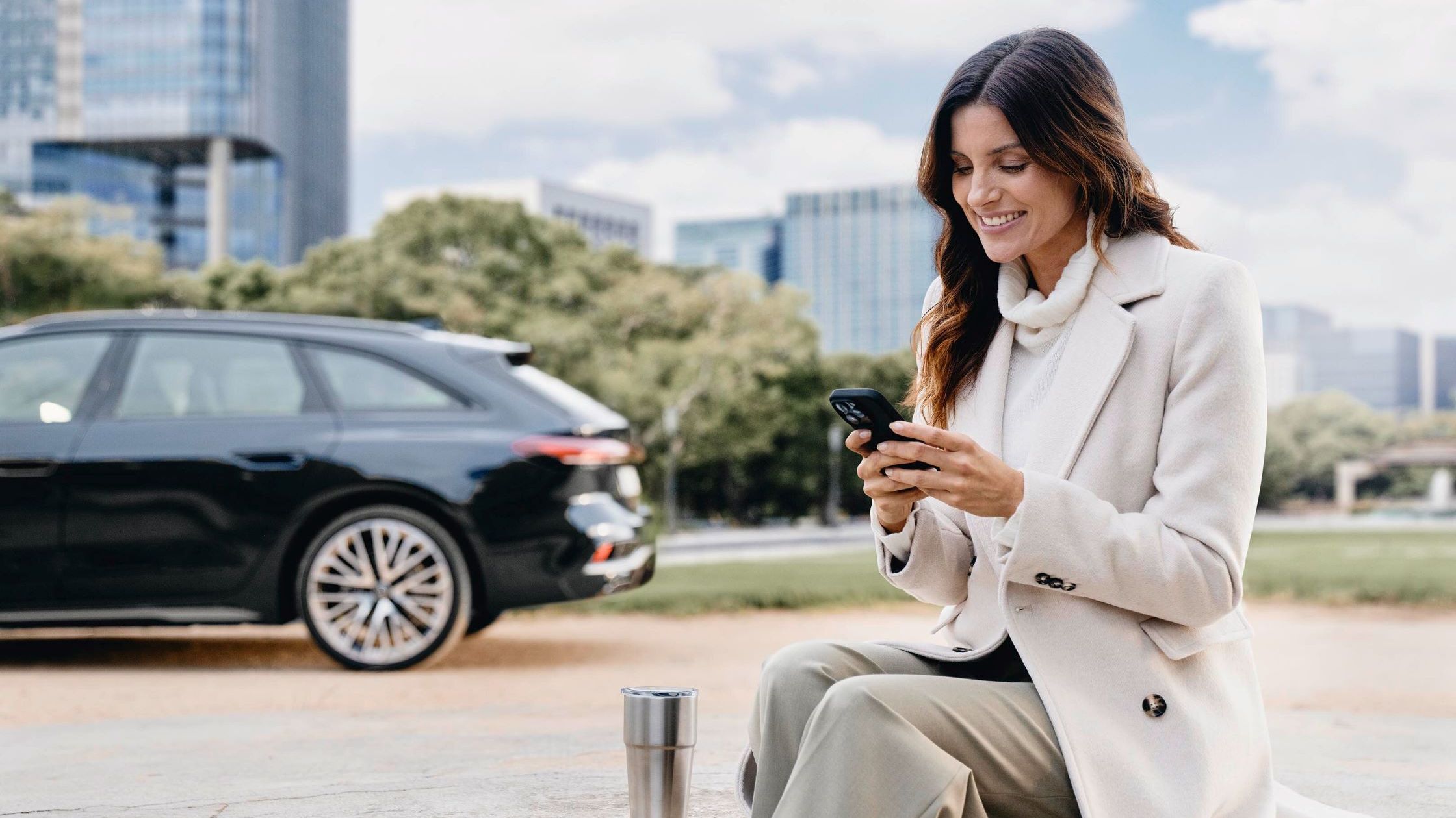 Eine Frau blickt auf ihr Smartphone, im Hintergrund ist ein Audi zu sehen.