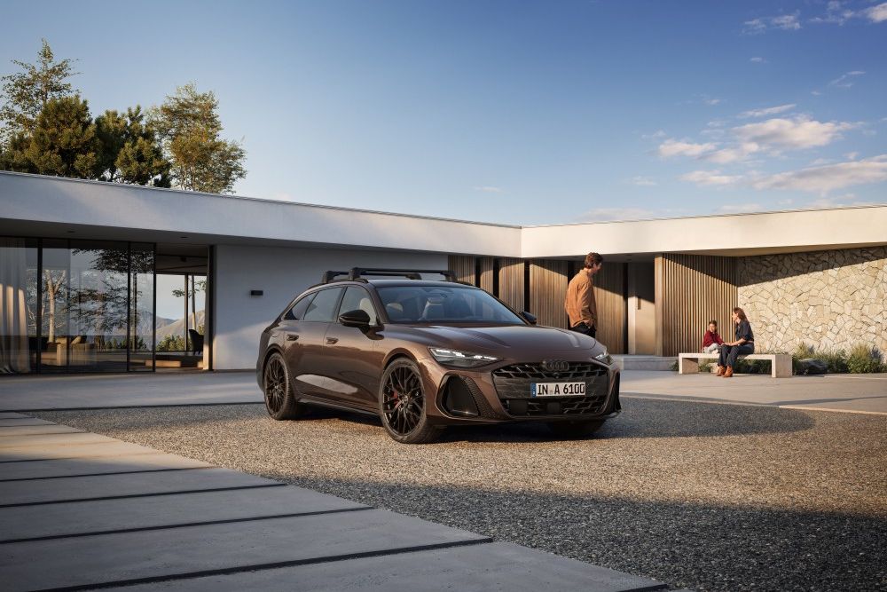 Mann lehnt an parkendem Audi A6 mit schwarzem Träger und schaut zu einer Frau und einem Kind, die auf einer Bank sitzen