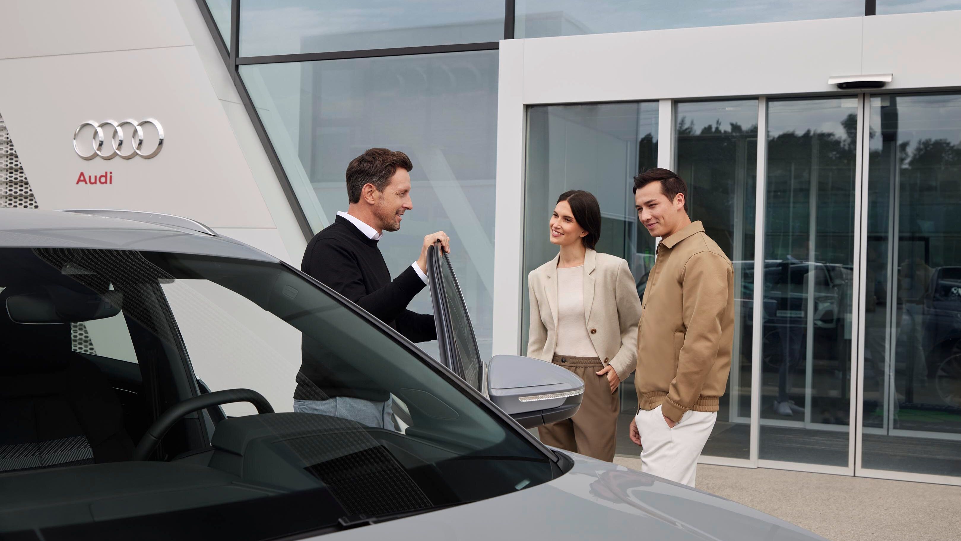 Ein Audi Service Mitarbeiter vor einem Audi im Kundengespräch.