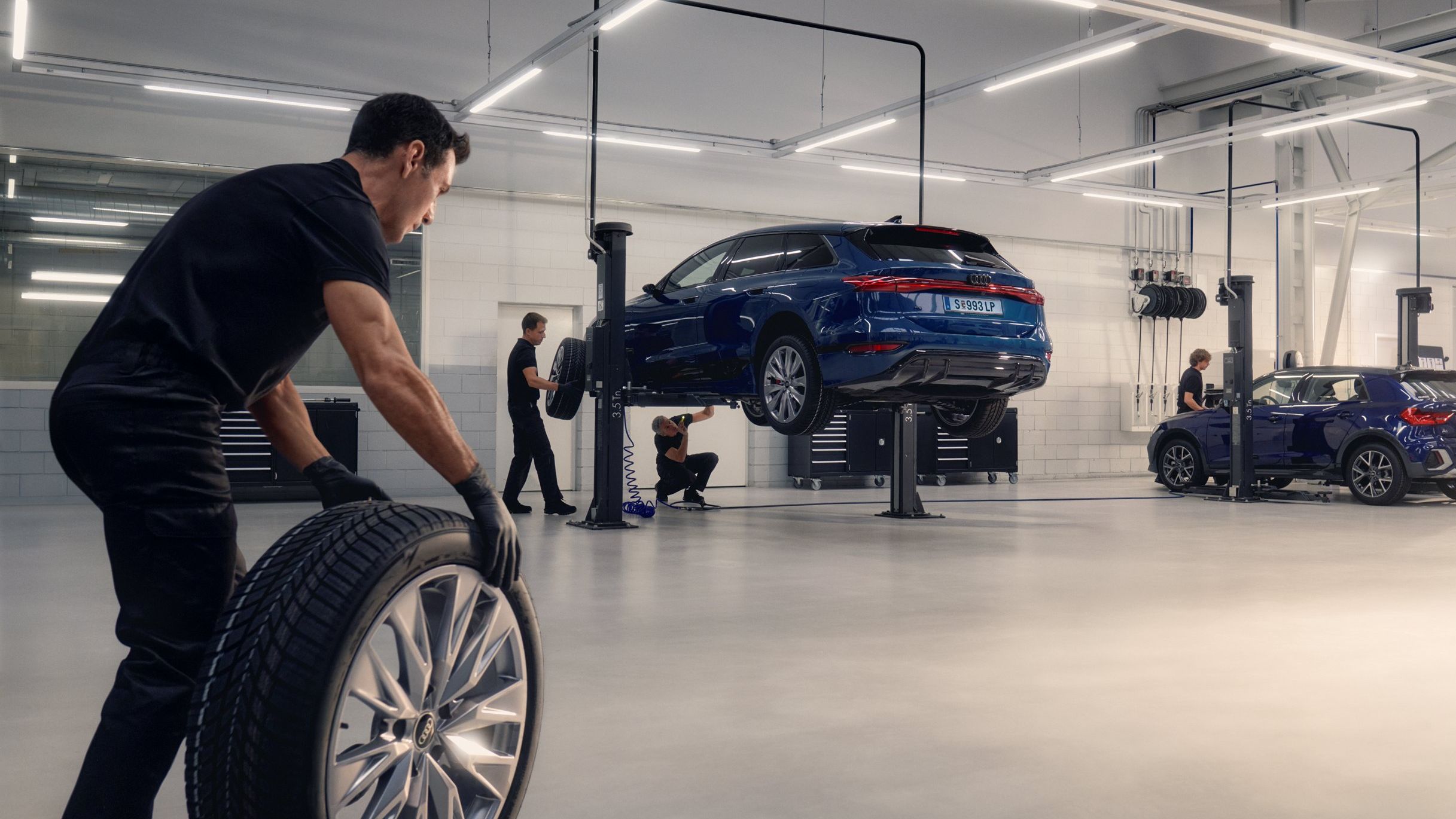 Ein Audi Mechaniker rollt ein Winterkomplettrad in Richtung eines Audi auf einer Hebebühne.