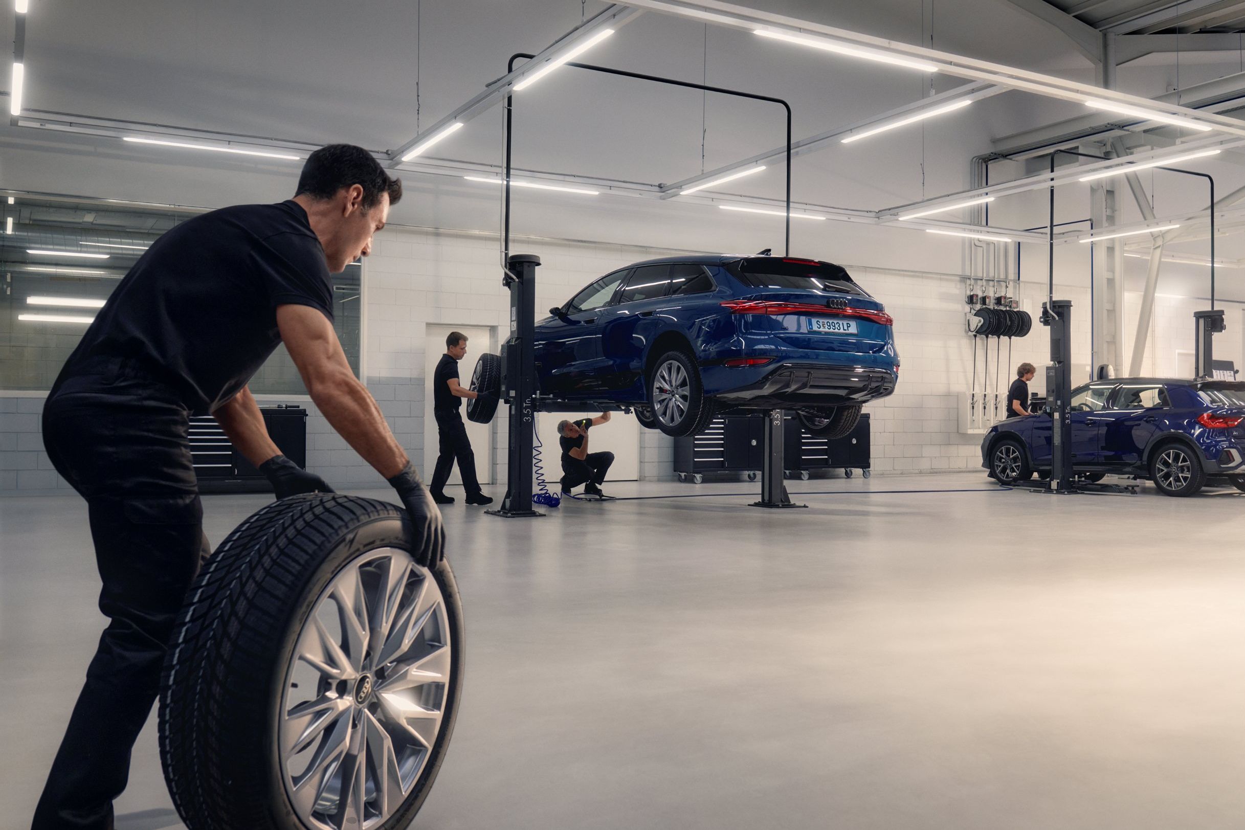 Ein Audi Mechaniker rollt ein Winterkomplettrad in Richtung eines Audi auf einer Hebebühne.