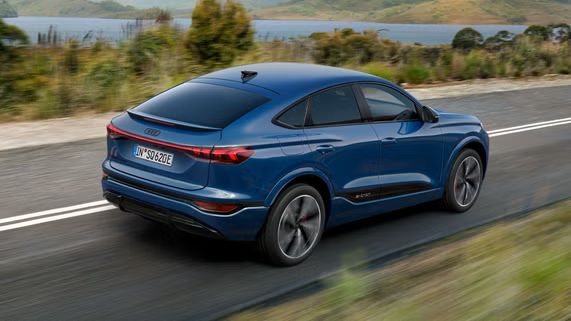 Schräge Heckaufnahme des SQ6 Sportback e-tron, welcher eine Straße an einem See in einer bergigen Landschaft entlangfährt.