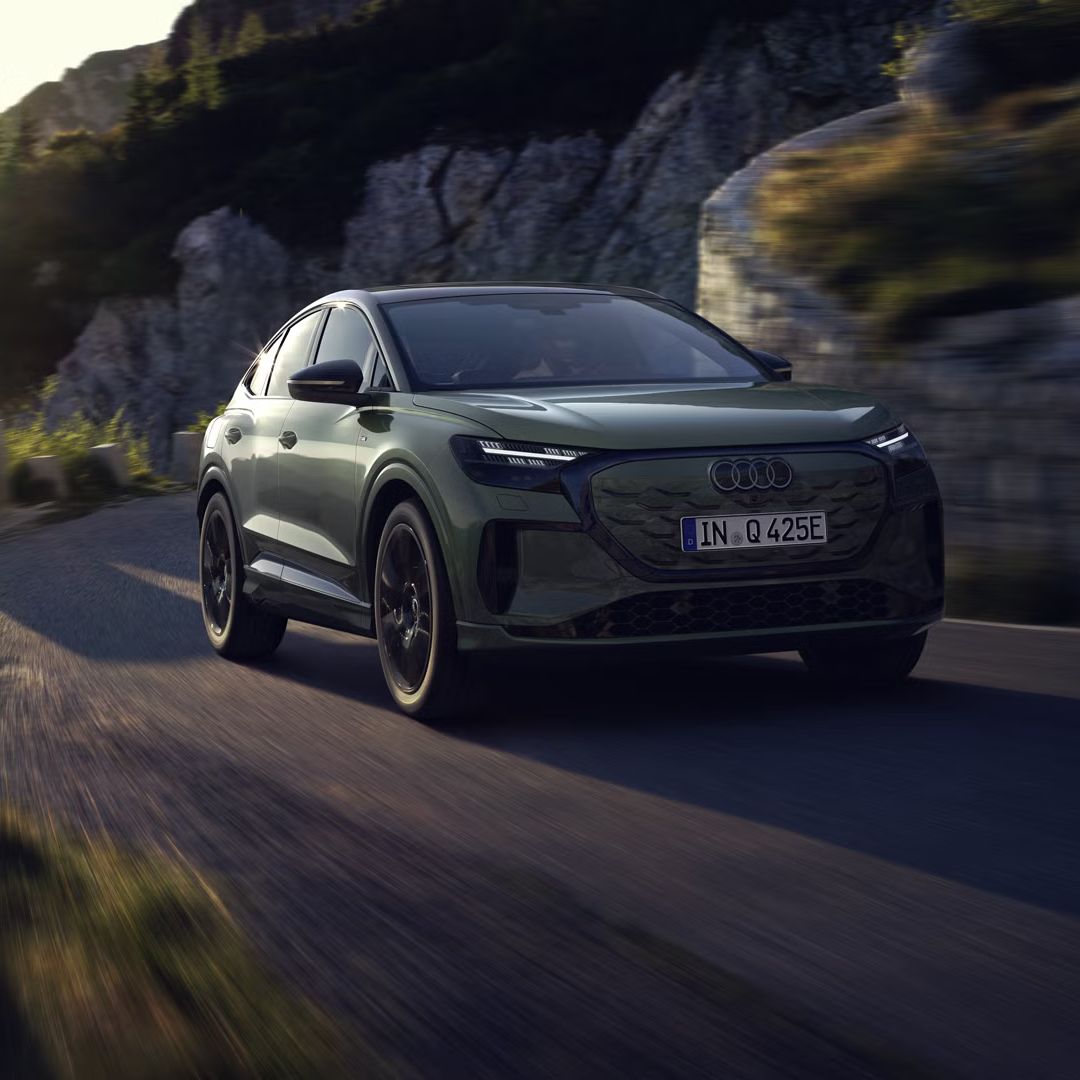 Der Q4 Sportback e-tron bei der Fahrt auf einer Bergstraße. Sonnenstrahlen von links oben beleuchten das Bild, das Fahrzeug wirft Schatten nach vorne.