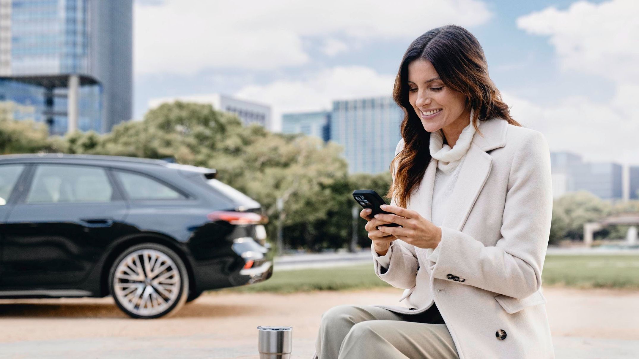Eine Frau blickt auf ihr Smartphone, im Hintergrund ist ein Audi zu sehen.