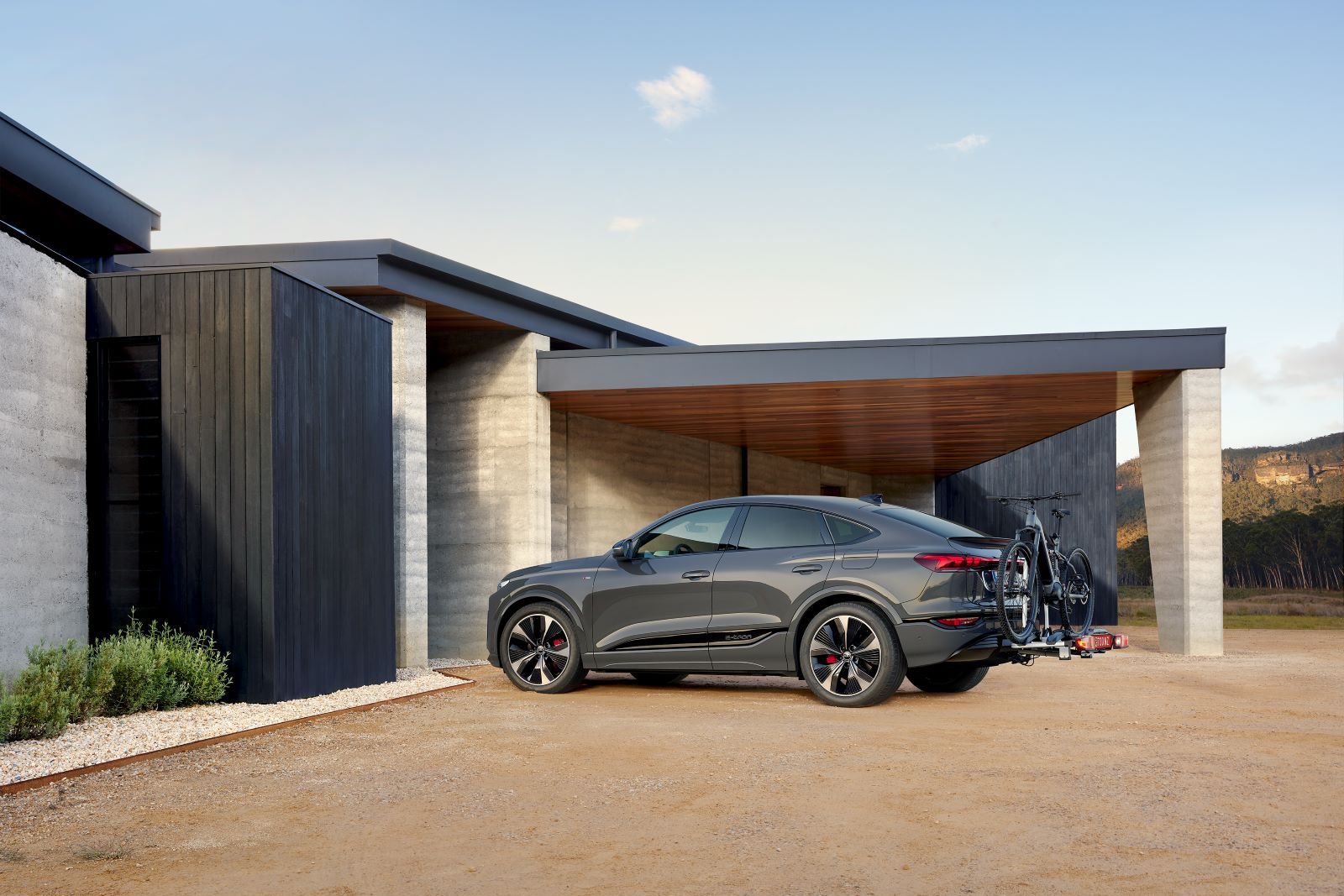 Ein Audi Q6 mit Fahrradheckträger parkt vor einem Haus.