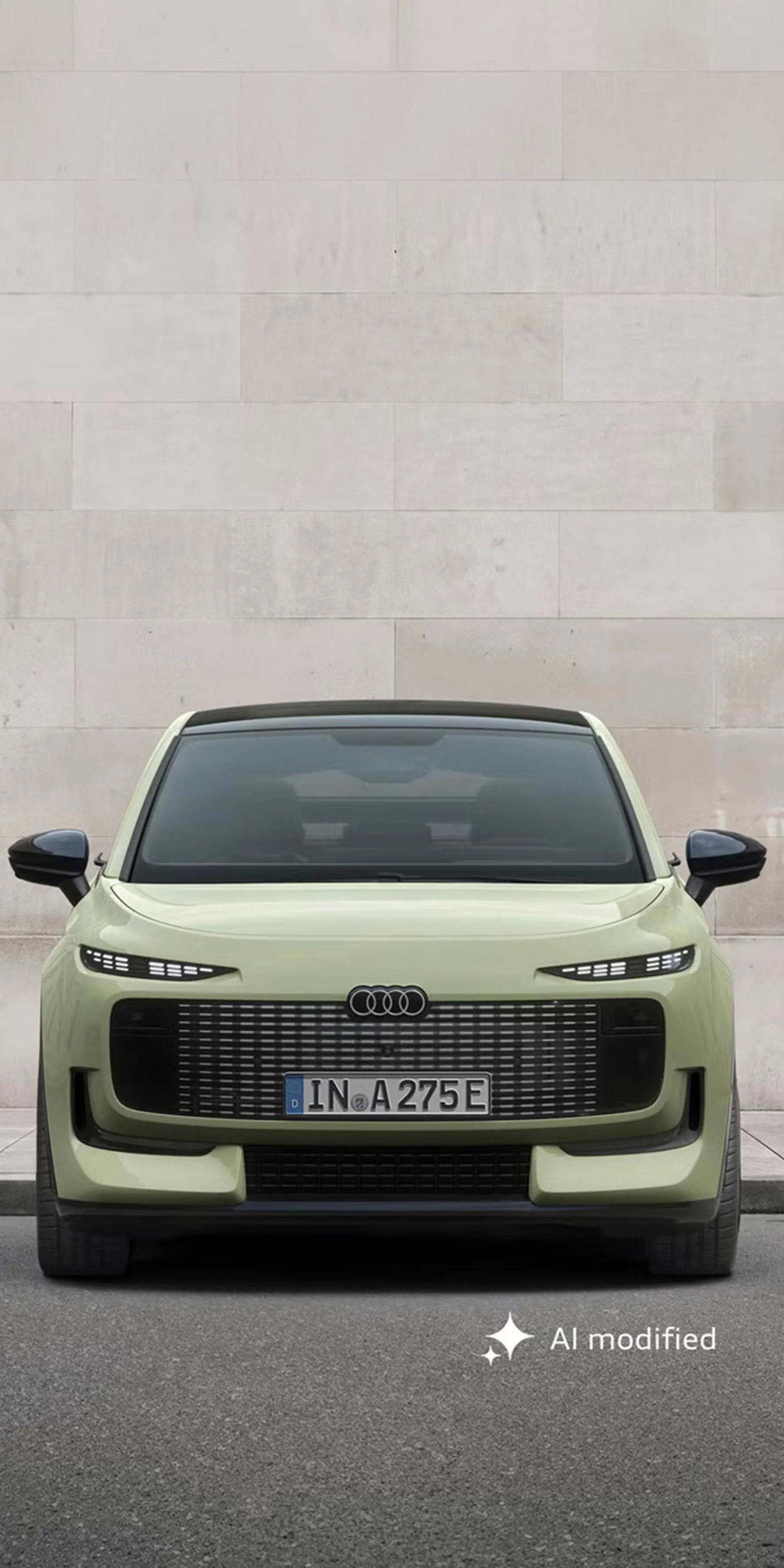 Der Audi A2 e-tron frontal von vorn auf einem Parkplatz, dahinter eine Gebäudewand in Steinoptik.