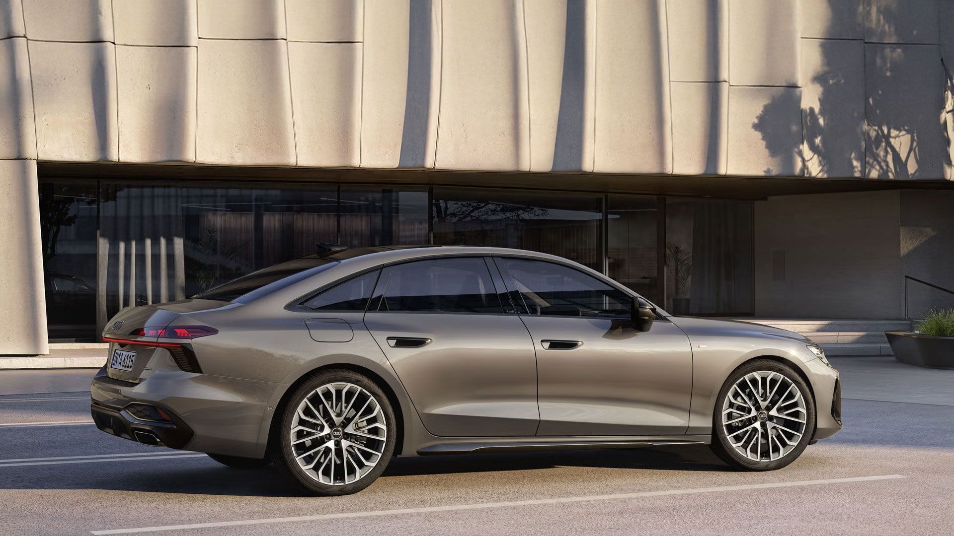 Die A6 Limousine in Dakotagrau Metallic steht im Seitenprofil auf einem Parkplatz vor einem großen, modernen Gebäude.