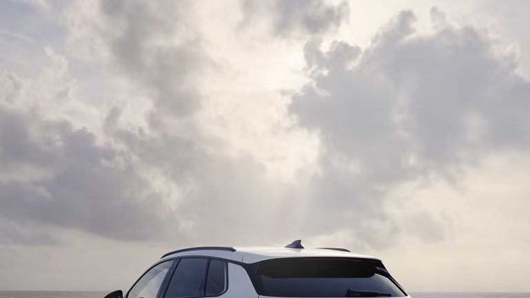 Ein weißer Q3 SUV e-hybrid von hinten fährt auf nasser Straße entlang der Küste.	