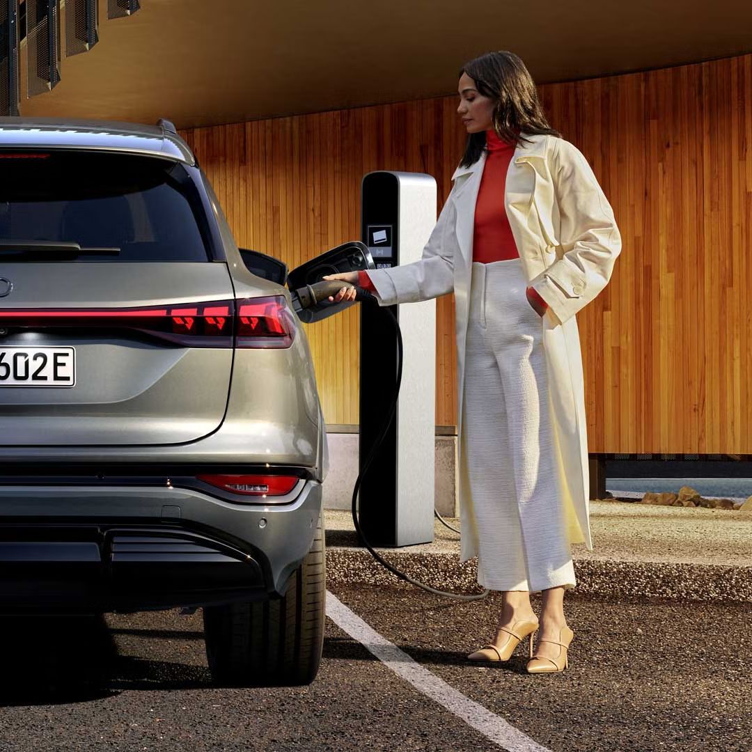 Der SQ6 SUV e-tron steht auf einem Parkplatz vor einer Gebäudefassade und wird von einer jungen Frau an eine Ladestation angeschlossen.