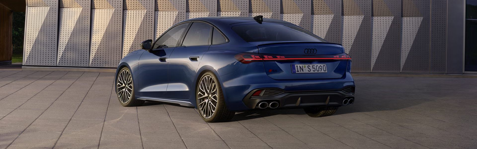 Die S5 Limousine in dunkelblau steht schräg vor einer Gebäudefassade und wird dabei vom Sonnenlicht angestrahlt.