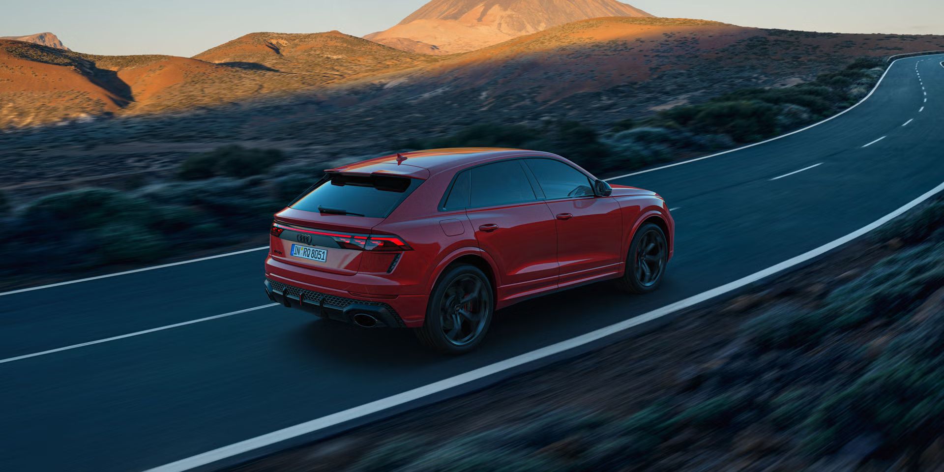 Der RS Q8 SUV performance von schräg hinten auf einer Bergstraße. Die Sonne beleuchtet die felsige Landschaft im Hintergrund, das Fahrzeug im Schatten.