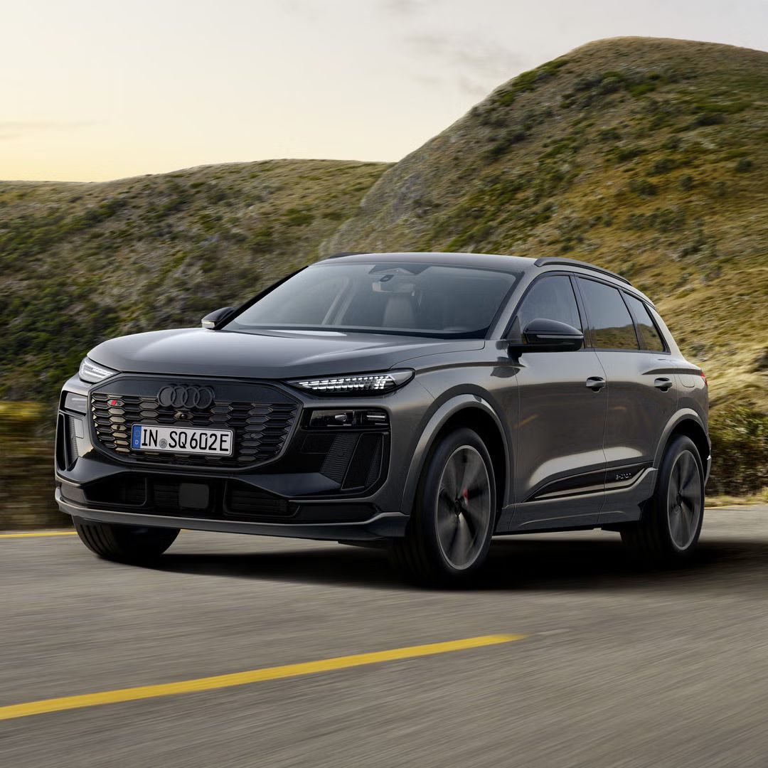 Seitliches Frontprofil des SQ6 SUV e-tron, welcher über eine Landstraße in bergiger Umgebung fährt.