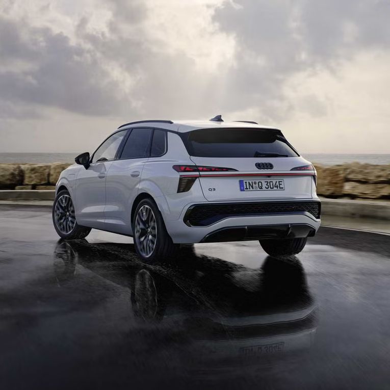 Ein weißer Q3 SUV e-hybrid von hinten fährt auf nasser Straße entlang der Küste.	