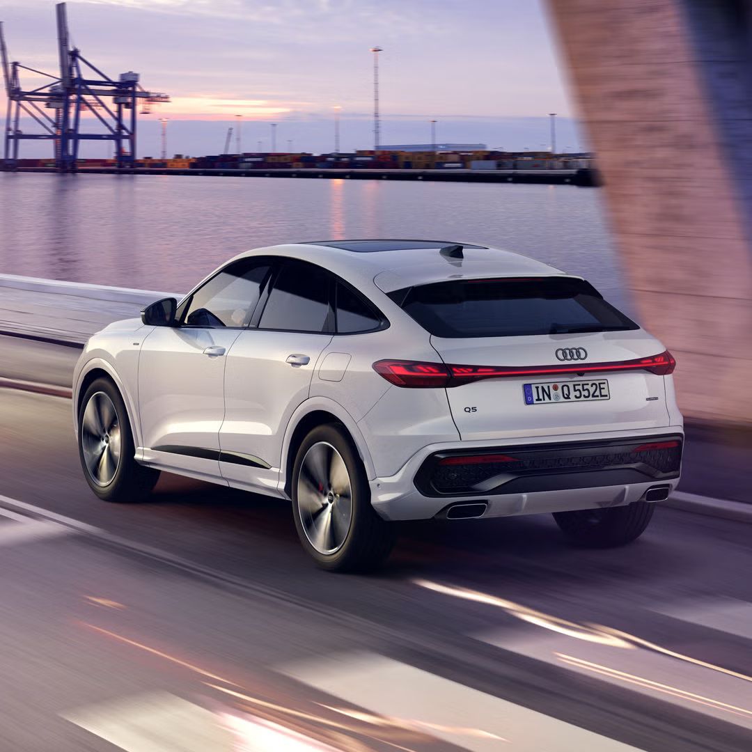 Der Q5 Sportback in schräger Heckperspektive, während er bei Dämmerung eine Hafenstraße entlangfährt.