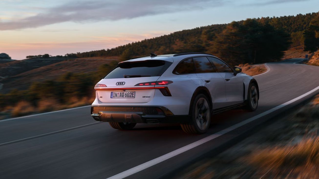 Der Audi A6 allroad e-hybrid schräg von hinten in voller Fahrt auf einer Gebirgsstraße. Im Hintergrund ein Waldstück.
