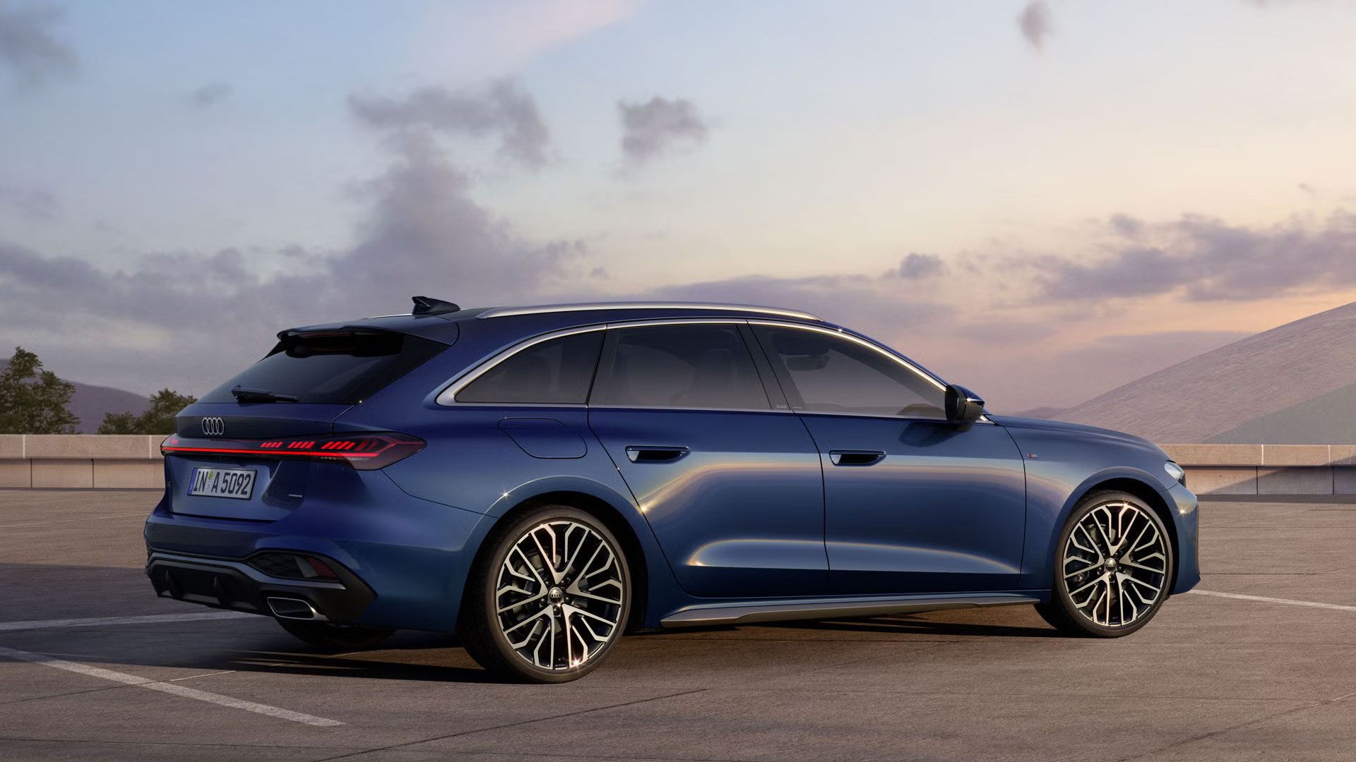 Der A5 Avant in Ascariblau Metallic steht im schrägen Seitenprofil auf einem großen Parkplatz. 