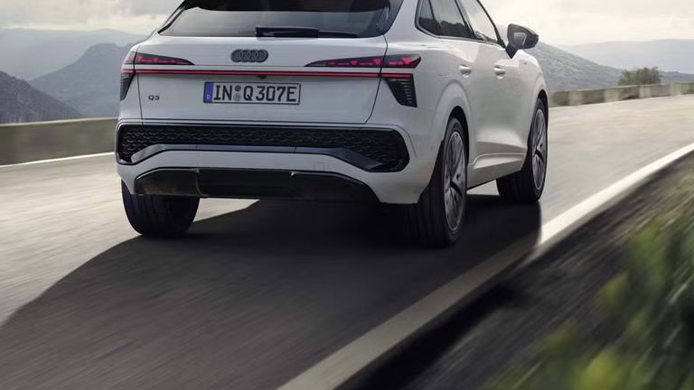 Ein weißer Q3 Sportback e-hybrid fährt auf einer Landstraße in einer bergigen Landschaft.	