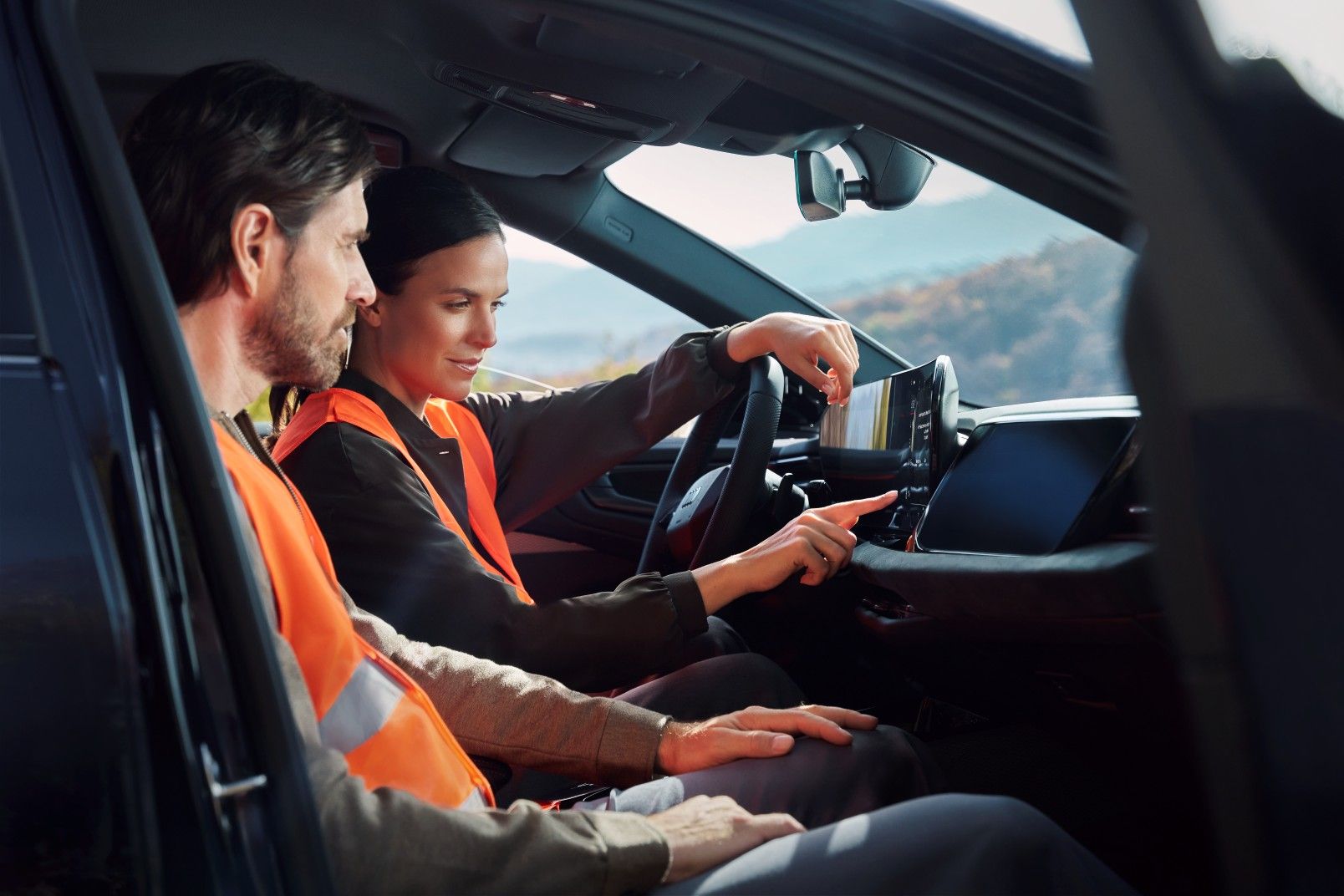Ein Mann und eine Frau mit Warnweste sitzen in einem Audi. Die Frau bedient den Touch Screen des Audi.