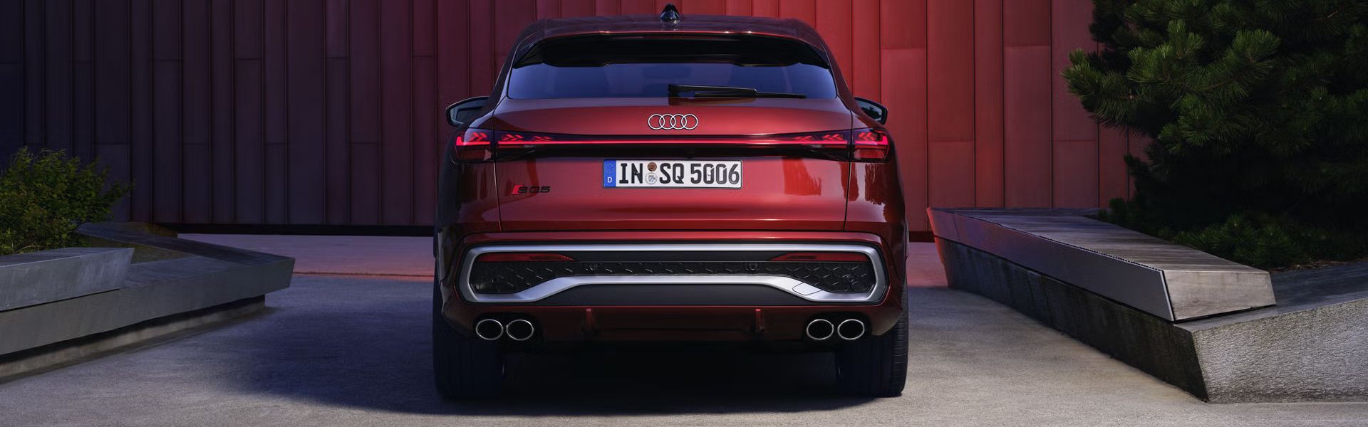Heckprofil des roten SQ5 Sportback vor einer Gebäudefassade, die vom Fahrzeug rot angeleuchtet wird.