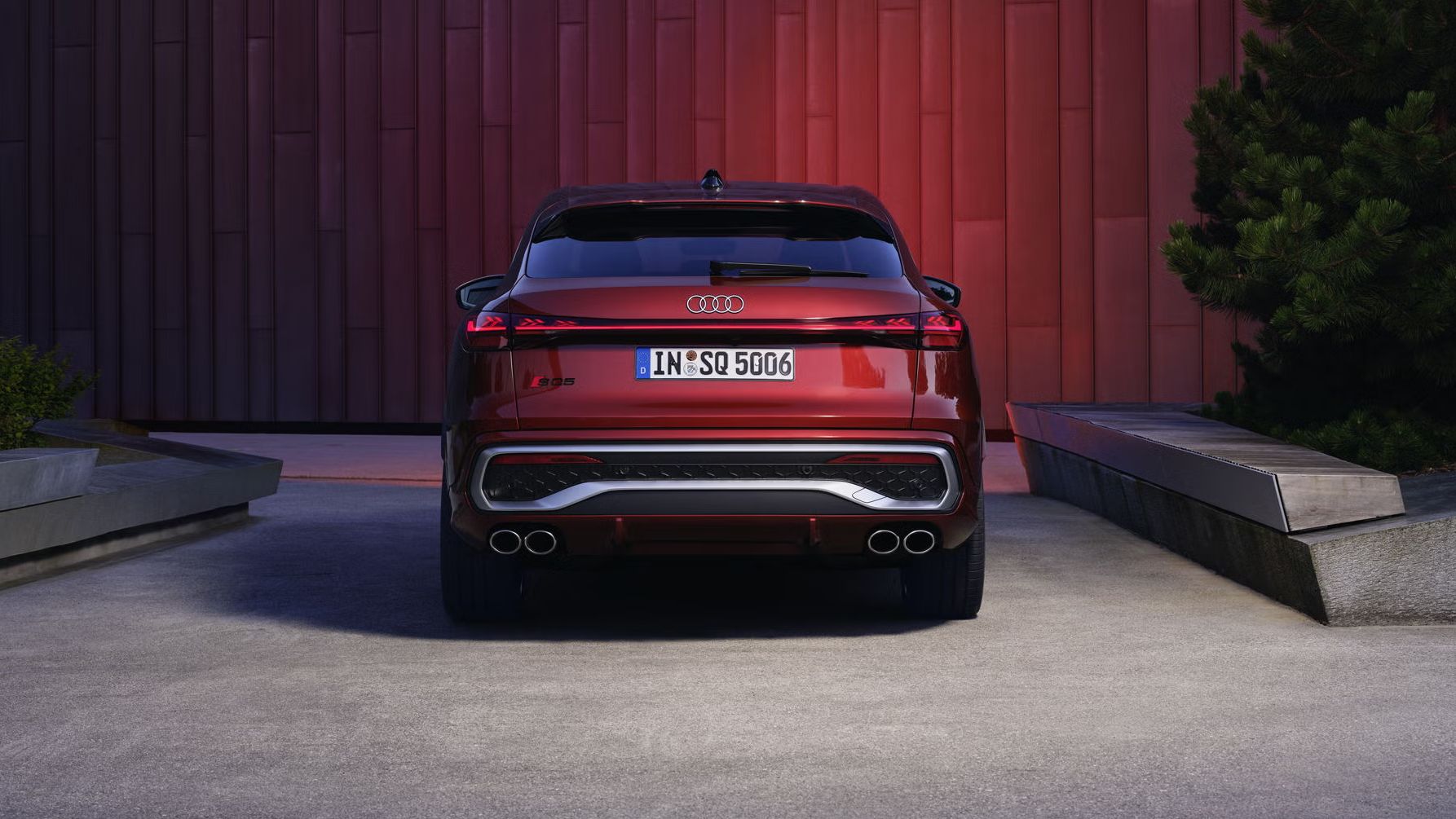 Heckprofil des roten SQ5 Sportback vor einer Gebäudefassade, die vom Fahrzeug rot angeleuchtet wird.