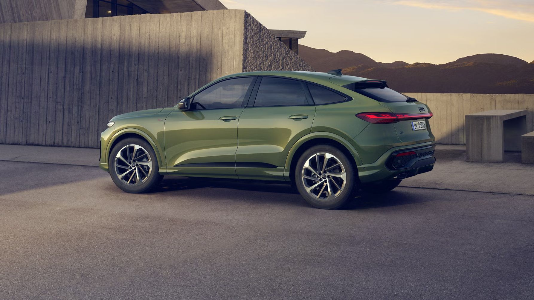 Ein grüner Q5 Sportback in Seitenansicht steht auf einem Parkplatz vor einem urbanen Haus in bergiger Umgebung.
