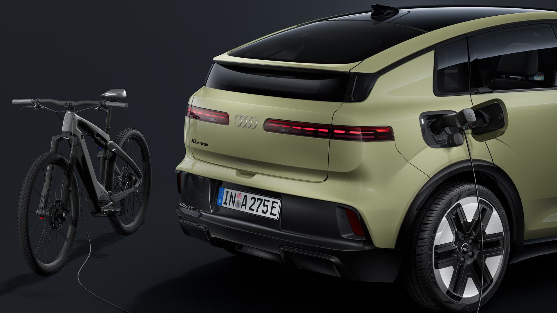 Nahaufnahme des Hecks. Am geöffneten Ladeanschluss des Audi A2 e-tron ist ein Stromkabel angeschlossen, welches ein E-Bike hinter dem Fahrzeug lädt.