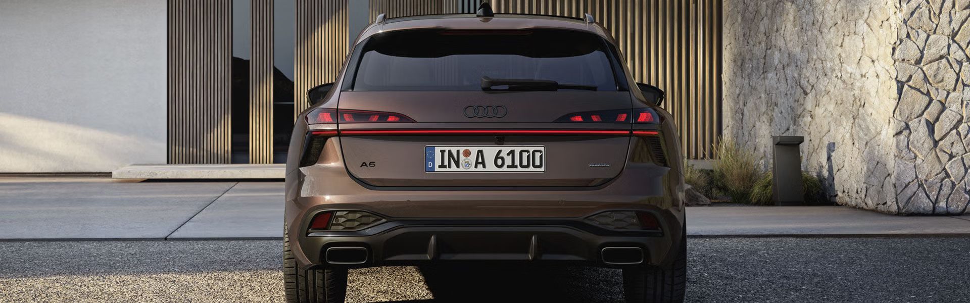 Heckaufnahme des A6 Avant, der auf einer Kiesfläche vor einer Fassade mit Holzvertäfelung und hohen Fenstern steht.