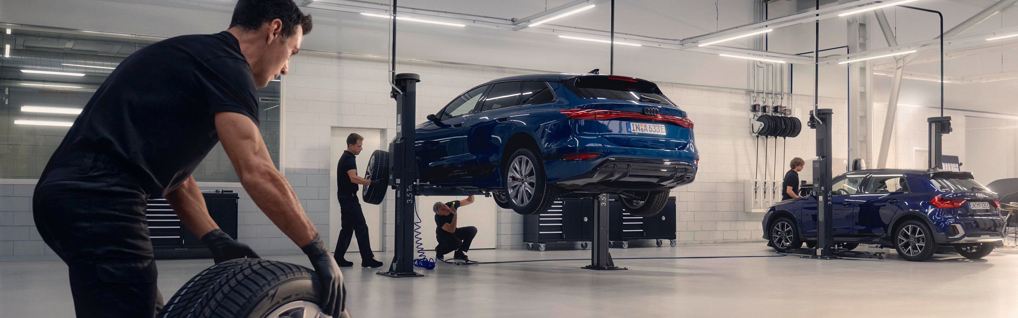 Ein Audi Mechaniker rollt ein Winterkomplettrad in Richtung eines Audi auf einer Hebebühne.