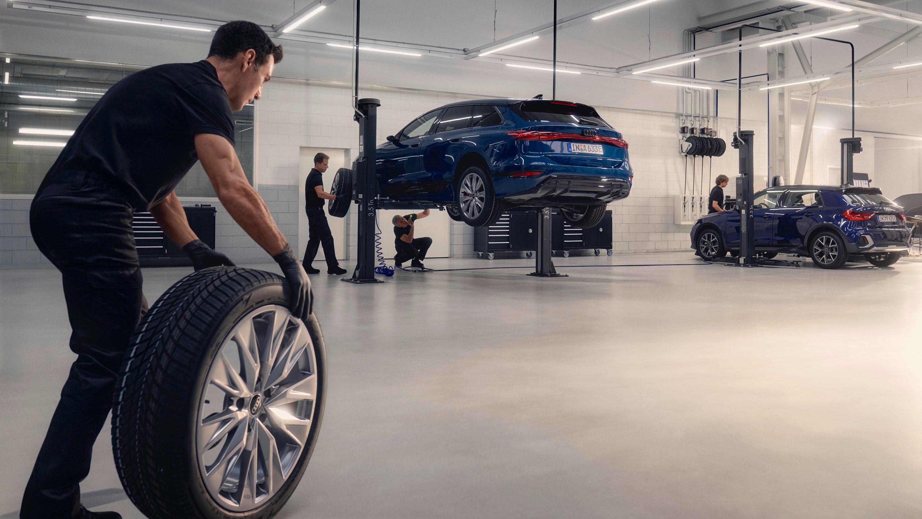 Ein Audi Mechaniker rollt ein Winterkomplettrad in Richtung eines Audi auf einer Hebebühne.